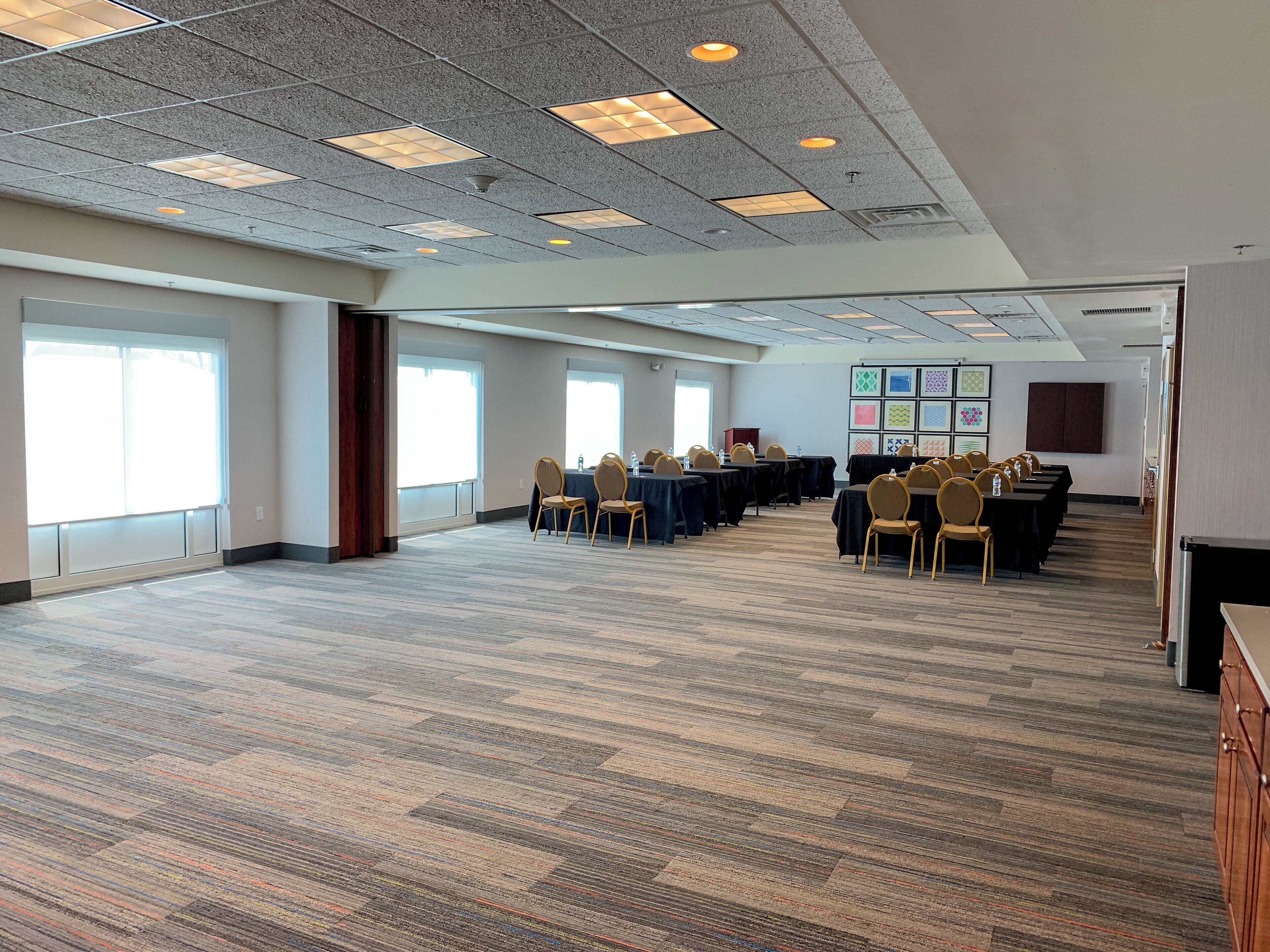 A conference room with a high ceiling, large windows, and a carpeted floor.