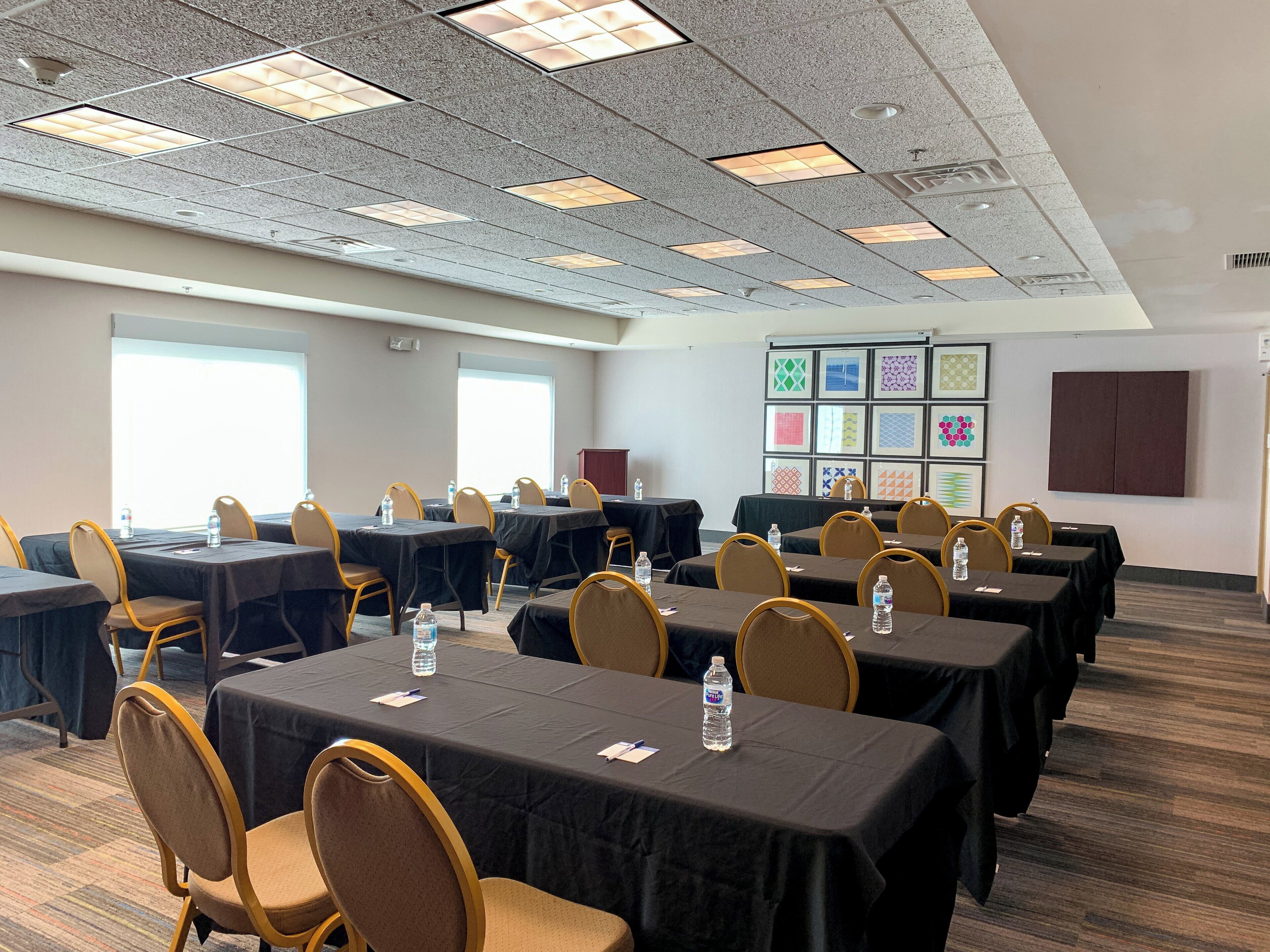 A conference room with multiple tables and chairs, equipped with water bottles, and a wall with framed artwork.