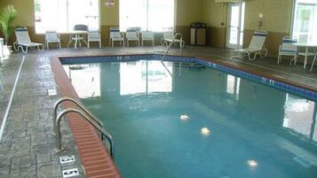 Ein Hallenbad mit klarem Wasser, umgeben von Liegestühlen und einem Steinboden.
