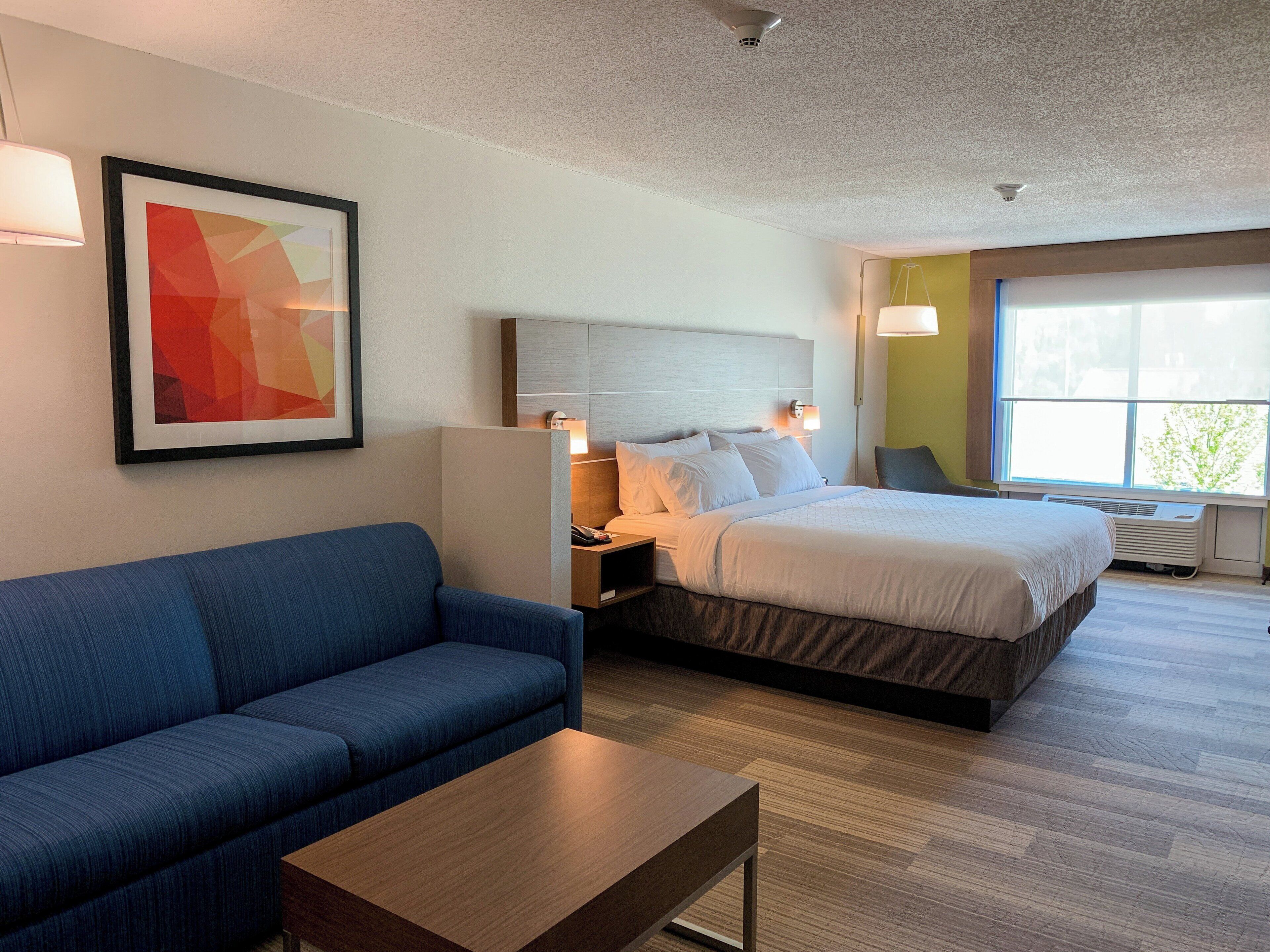 A hotel room with a bed, a blue sofa, a wooden table, and a framed abstract painting.
