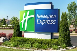 Une enseigne Holiday Inn Express aux couleurs vert et bleu, entourée d’un aménagement paysager verdoyant et d’arbres.