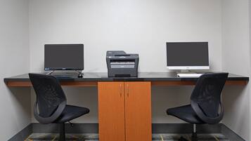 Un espacio de oficina moderno con dos sillas de oficina negras, un escritorio con dos monitores, una impresora y un armario de madera.