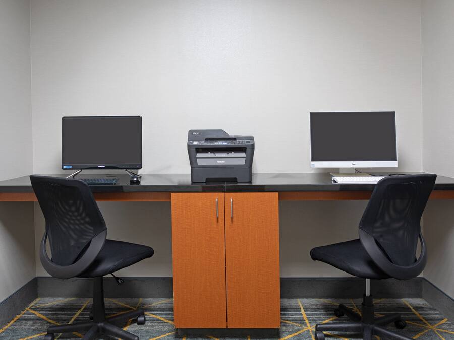 Um espaço de escritório moderno com duas cadeiras de escritório pretas, uma mesa com dois monitores, uma impressora e um armário de madeira.