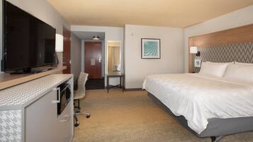 A hotel room with a bed, a desk with a chair, a television, and a framed artwork on the wall.