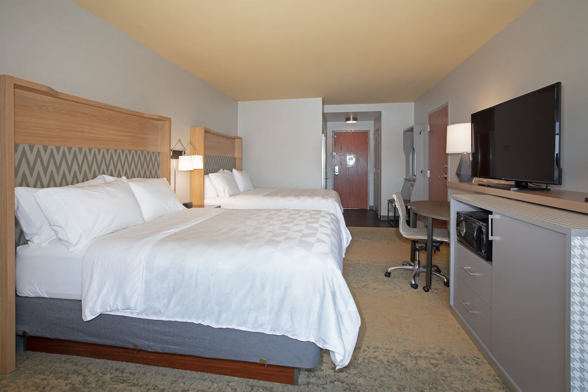 A hotel room with two beds, a desk, a television, and a minibar.