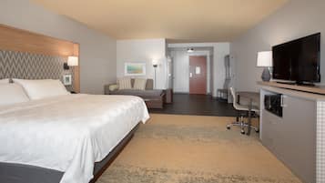 A hotel room with a large bed, a desk, a television, and a seating area.