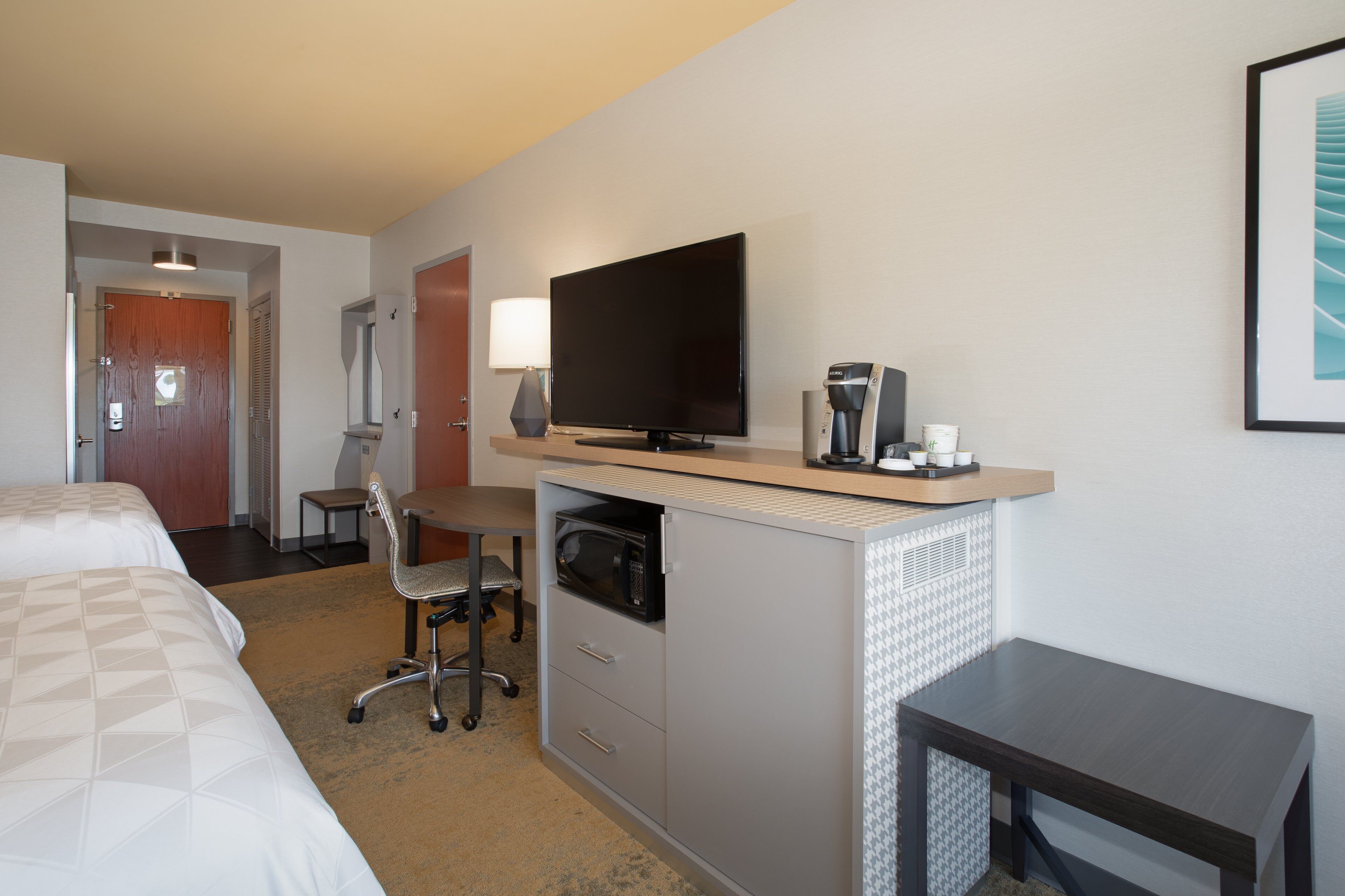 A hotel room with a bed, a desk with a television, a coffee machine, and a chair.