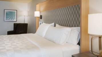 A hotel room with a bed, a chair, a lamp, and a wall-mounted picture.