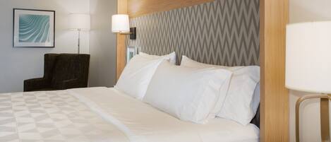 A hotel room with a bed, a chair, a lamp, and a wall-mounted picture.