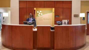 A reception desk with a wooden finish, a digital screen, and a sign indicating the hotel name.