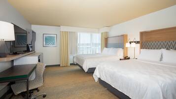 A hotel room with two beds, a desk, a chair, a TV, and a window with curtains.