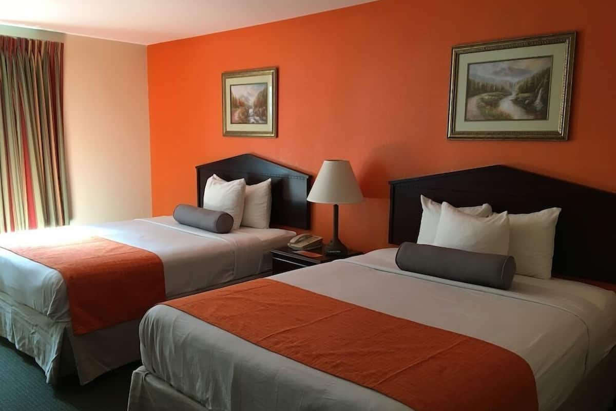 A hotel room with two beds, a nightstand, a lamp, and two framed pictures on the wall.