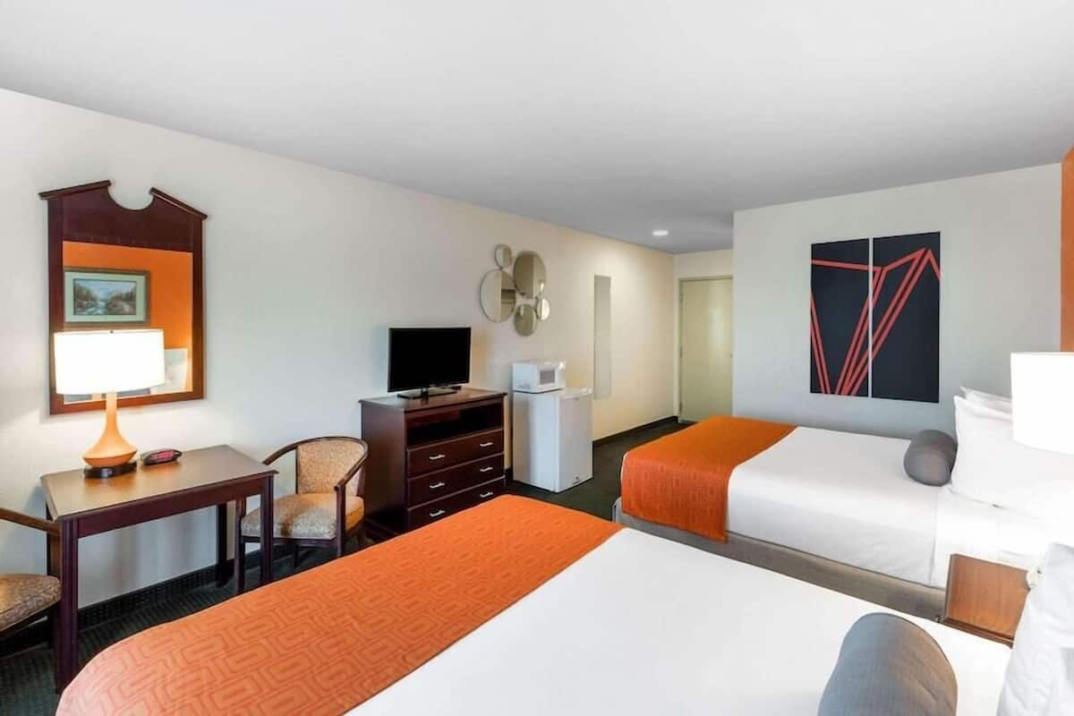 A hotel room with two beds, a desk with a lamp, a TV, a dresser, and a painting on the wall.