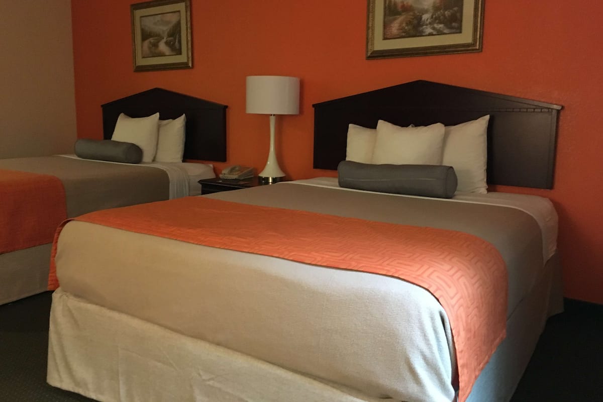 A hotel room with two beds, each with a headboard, a bedside table with a lamp, and two framed pictures on the wall.