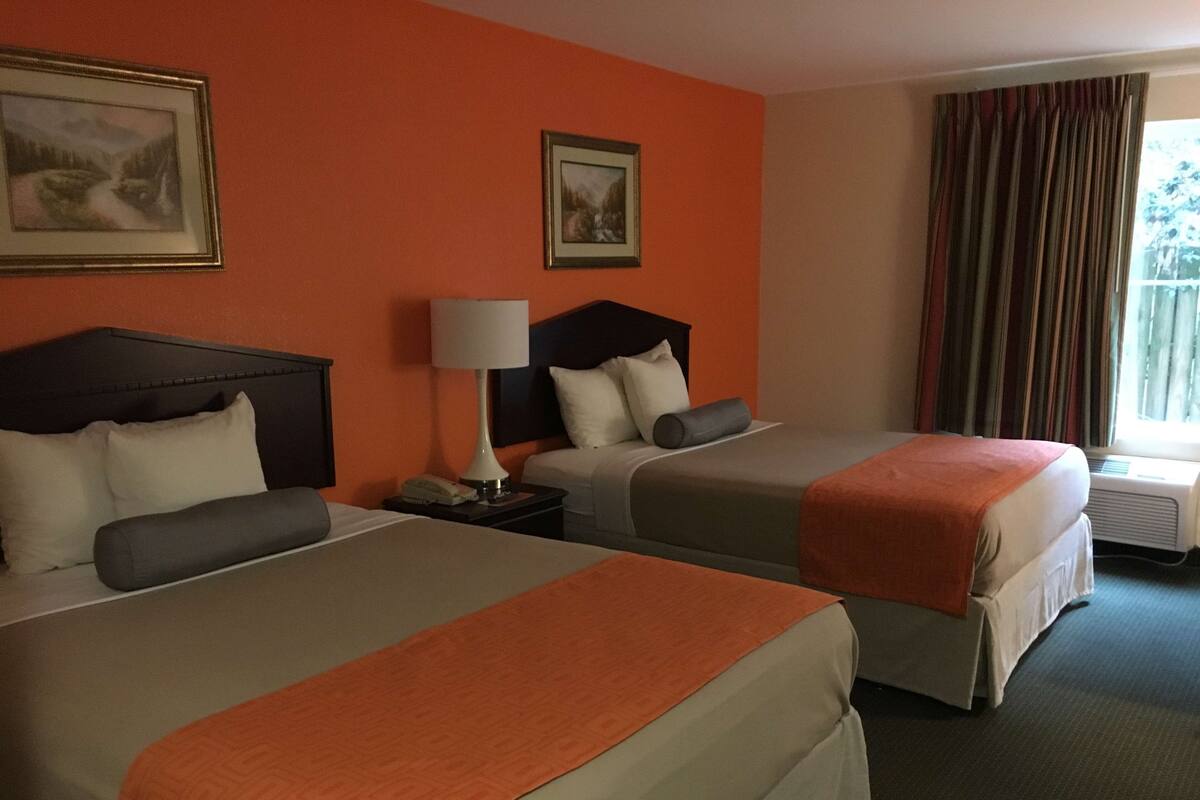 A hotel room with two beds, a nightstand with a lamp, and two framed pictures on the wall.