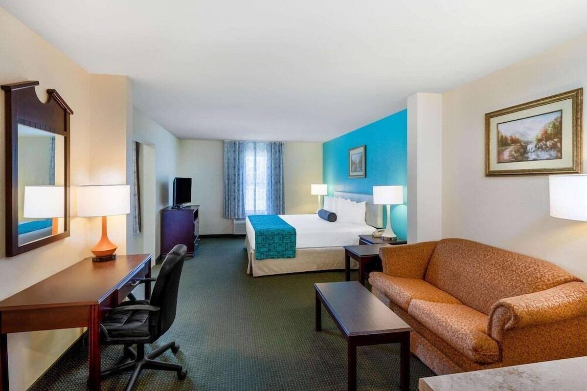A hotel room with a bed, desk, chair, couch, and two lamps.