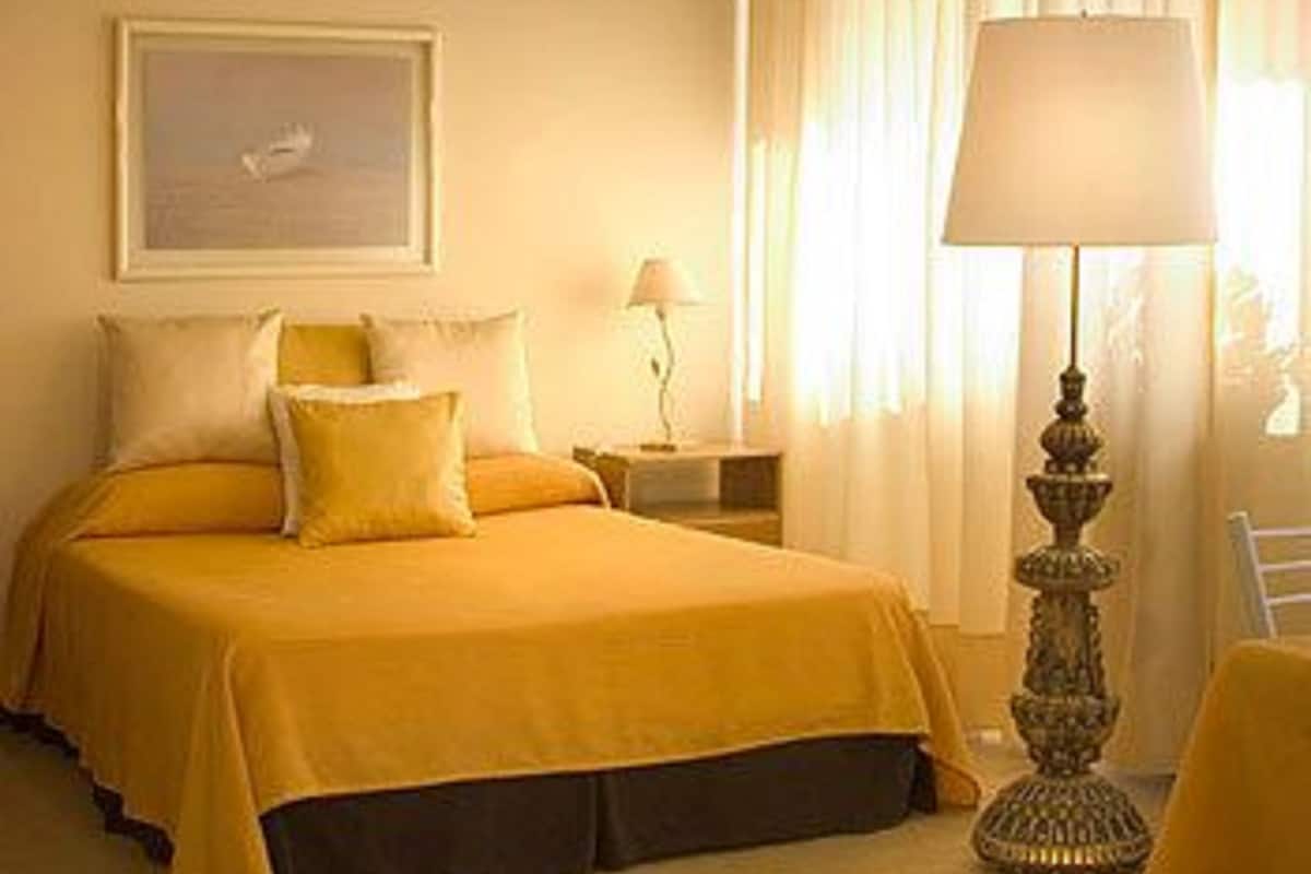 Habitación de hotel con cama, mesita de noche, lámpara y ventana con cortinas.