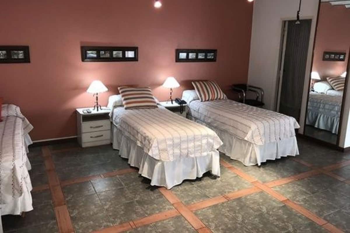 Una habitación con dos camas, un espejo, una silla y una mesita de noche con lámpara.