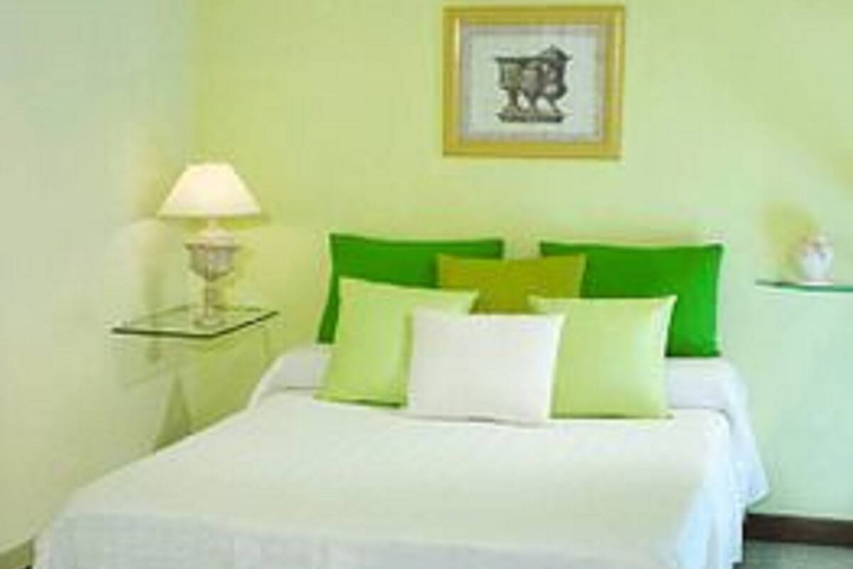 Un dormitorio ordenado con cama, almohadas y una mesita de noche con lámpara.