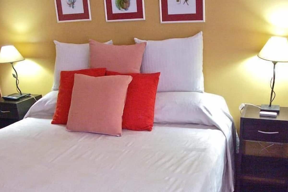Una habitación de hotel con una cama, dos mesitas de noche y lámparas de pared.
