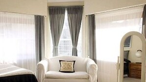Une chambre d’hôtel avec un lit, un fauteuil blanc, une coiffeuse et un grand miroir.