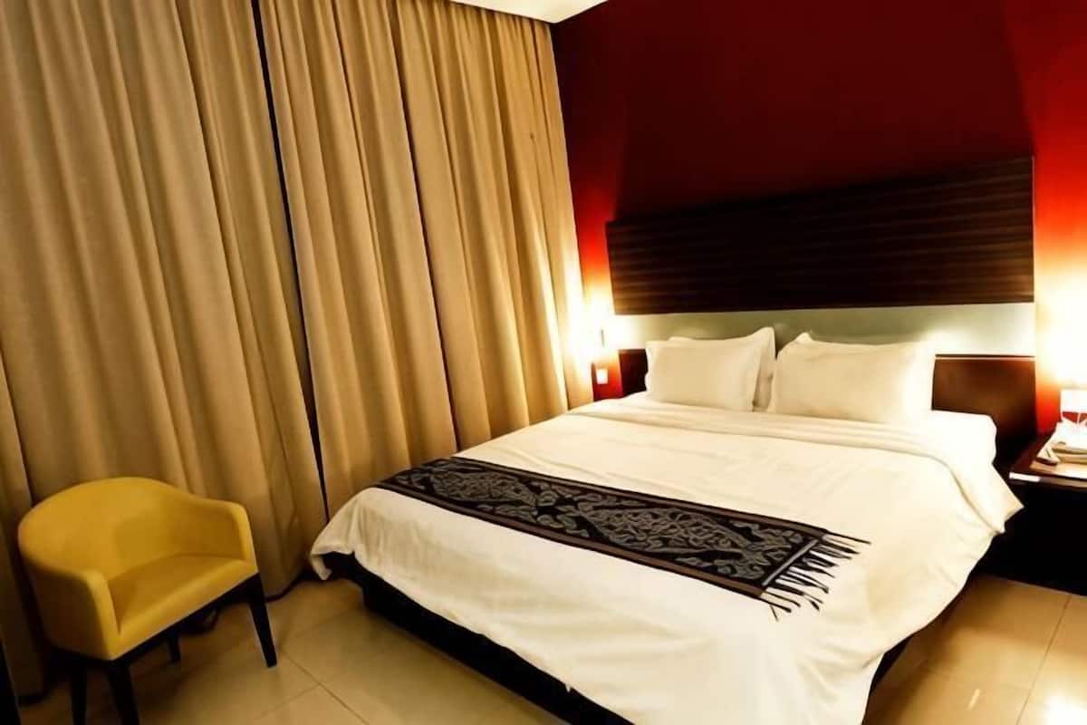 A hotel room with a bed, curtains, a nightstand, a lamp, and a chair.