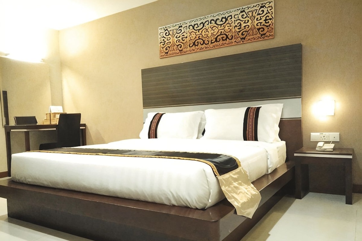 A hotel room with a large bed, bedside tables, a desk, and a decorative wall piece.