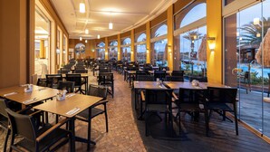 Un comedor interior amplio con varias mesas y sillas, y grandes ventanales que ofrecen vistas a una zona de piscina exterior.