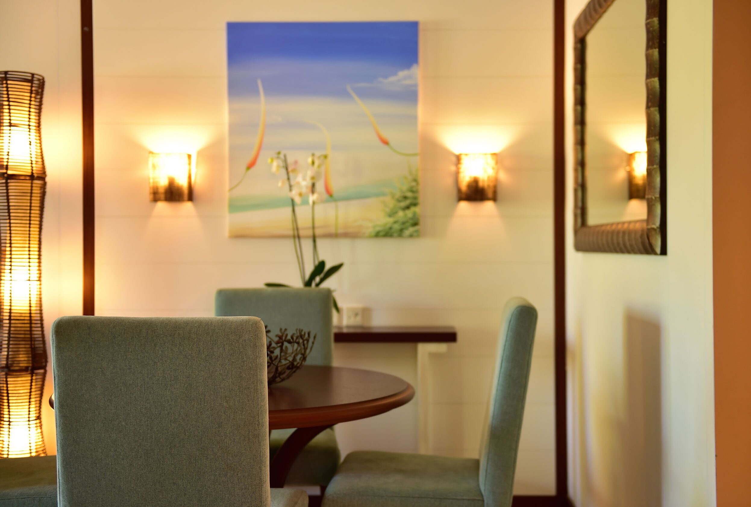 Un coin repas comprenant une table ronde, deux chaises, des appliques murales, un tableau et un miroir.