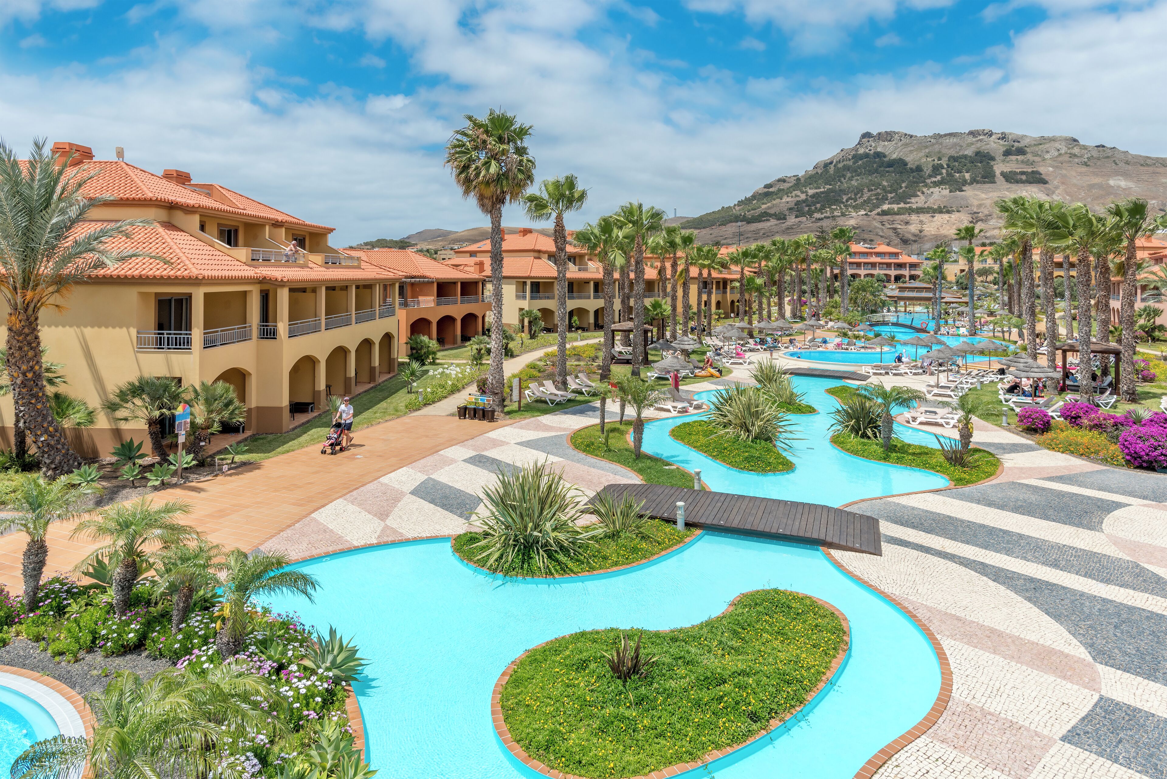 Un resort con varias piscinas, palmeras y montañas al fondo.