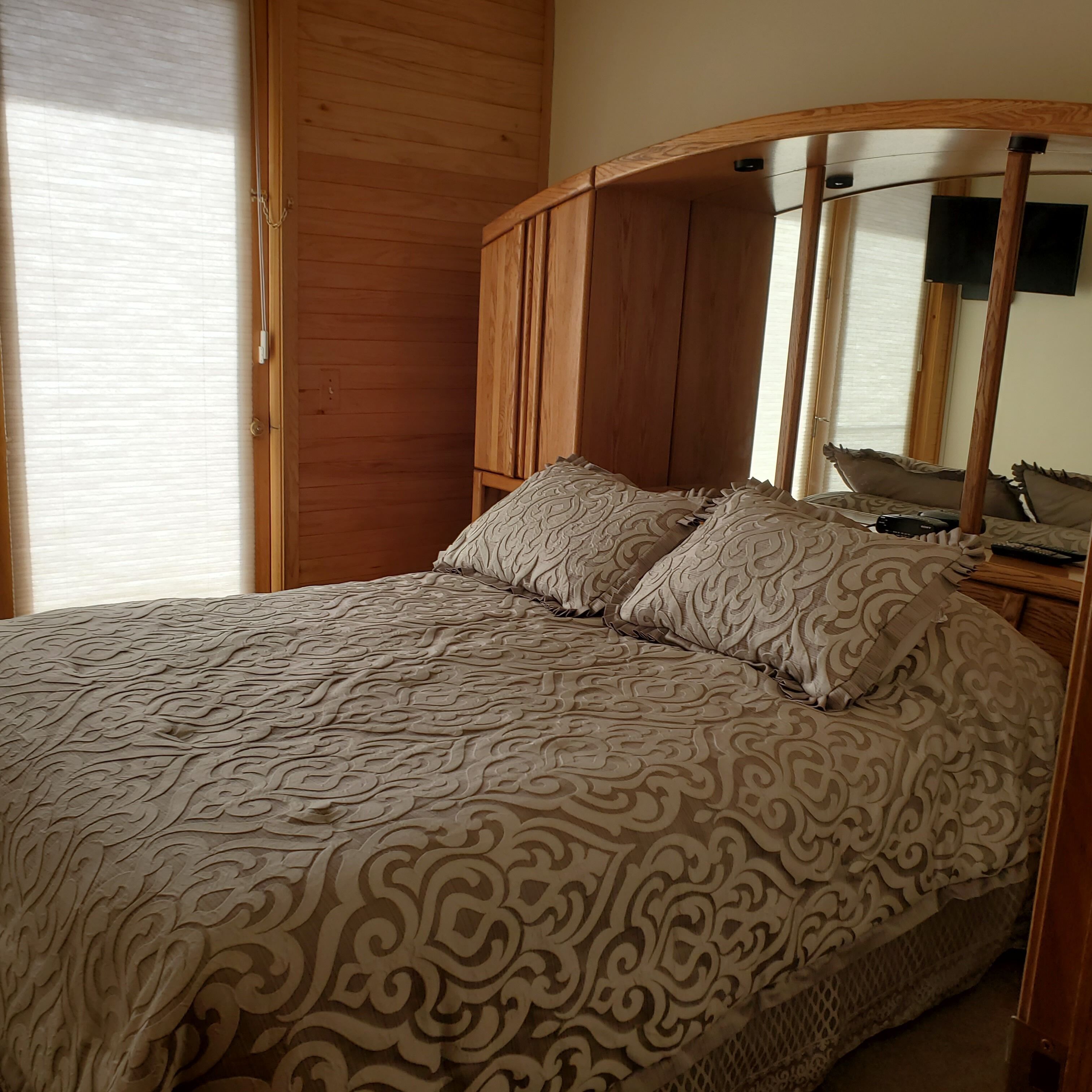 A bedroom with a bed, wooden wardrobe, and a television on a stand.