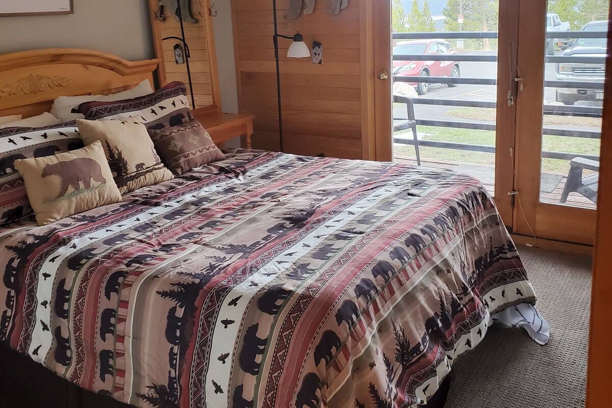 Un dormitorio con una cama grande, cabecera de madera y vista a un estacionamiento a través de una puerta abierta.