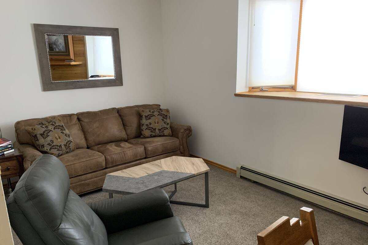 Un salón con un sofá de cuero marrón, un sillón de cuero negro, una mesita de centro de madera y un espejo grande en la pared.