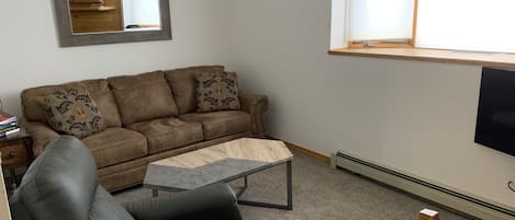A living room with a brown leather sofa, a black leather chair, a small wooden coffee table, and a large mirror on the wall.