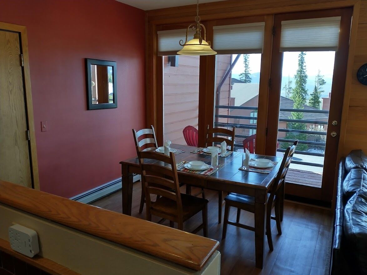 A dining area with a wooden table and chairs, a hanging light fixture, and a view of the outside through a sliding door.