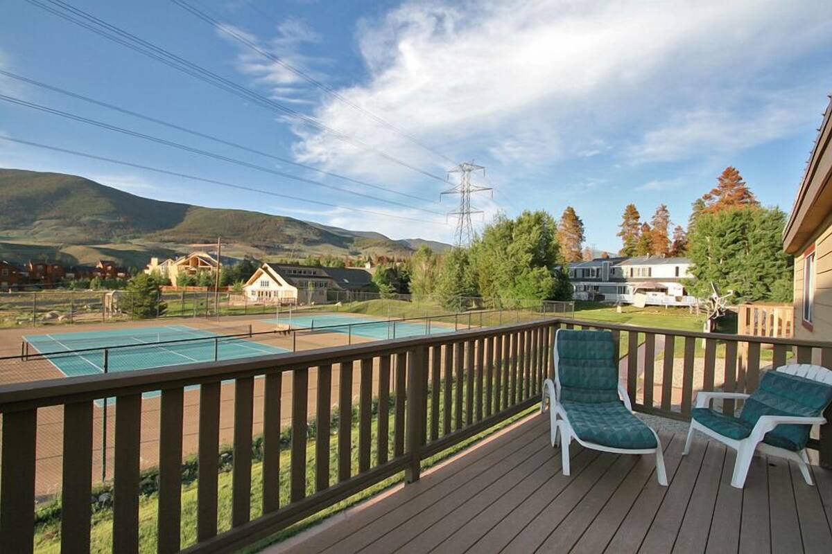 Una terraza con dos sillas Adirondack verdes, una cancha de tenis y vistas a casas y montañas.