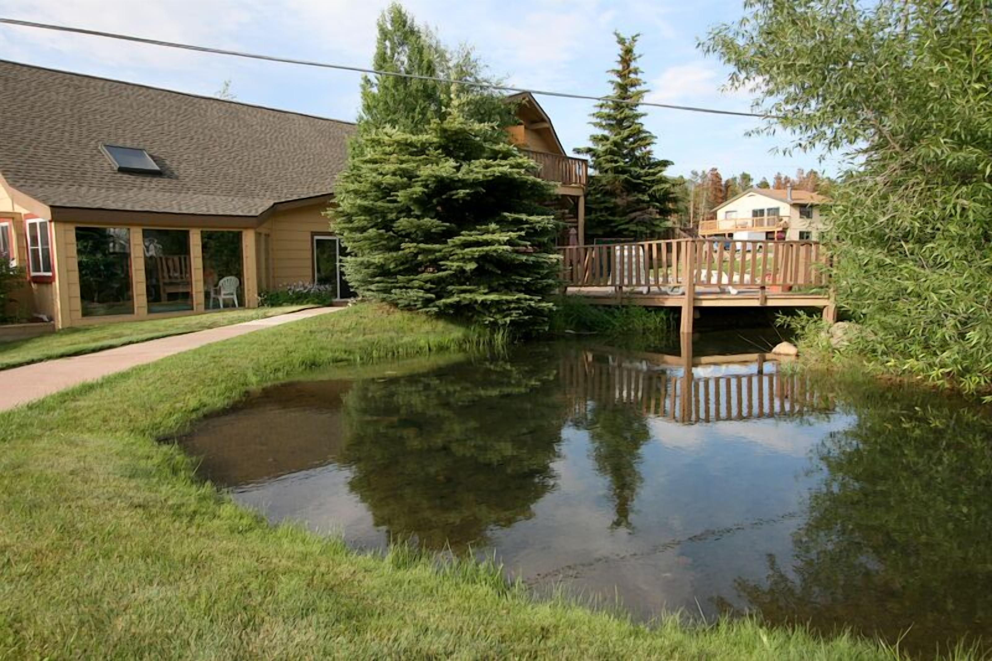 A building with a large glass window, a wooden deck, and a pond.