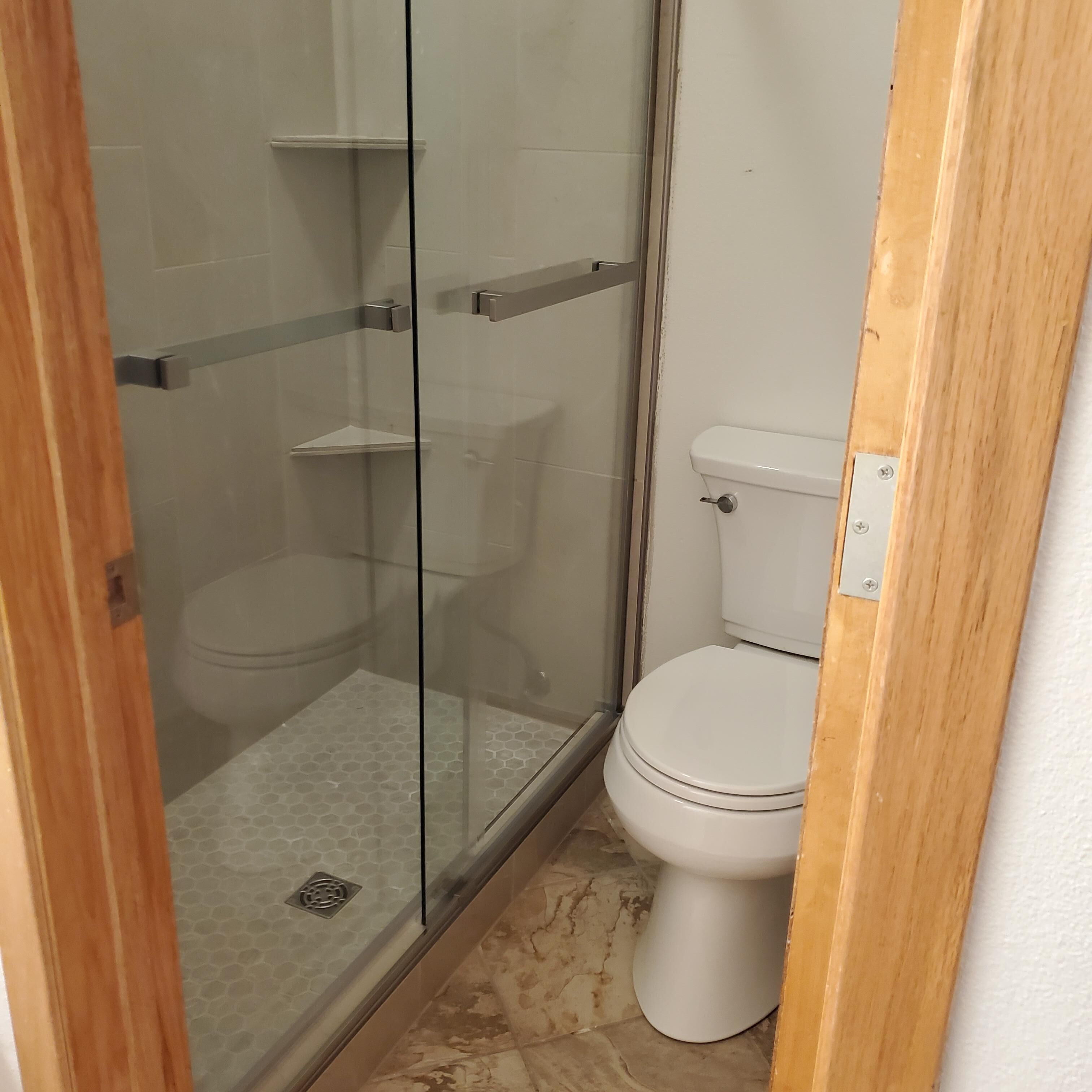 A bathroom with a glass-enclosed shower, a toilet, and a tiled floor.