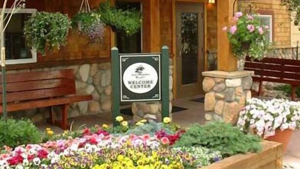 Ein hölzernes Gebäude mit einem Schild 'Welcome Center', Steinmauern, Bänken und Blumenbeeten.