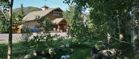 Eine rustikale Lodge mit einem Steinkamin, einer Holzterrasse und einem kleinen Bach im Vordergrund.
