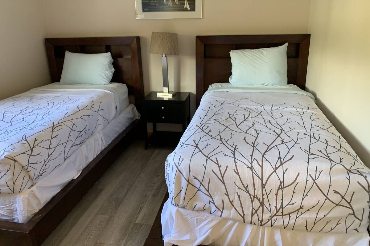 Dos camas individuales con cabeceros de madera, una mesita de noche con lámpara y un cuadro en la pared.