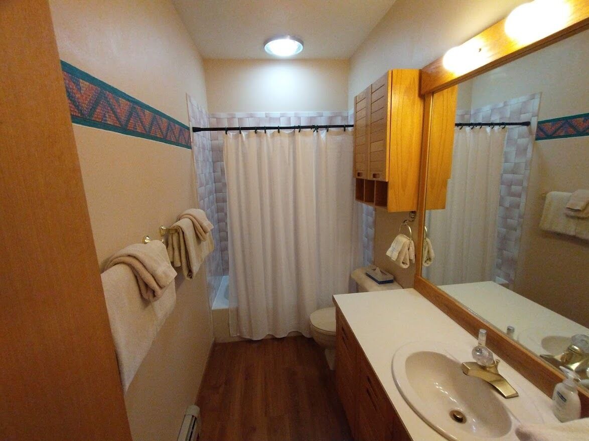 A bathroom with a wooden vanity, a sink, a toilet, and a shower curtain.
