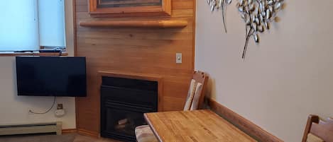 Una sala de estar acogedora con chimenea, paneles de madera, una mesa de comedor y un televisor montado en la pared.