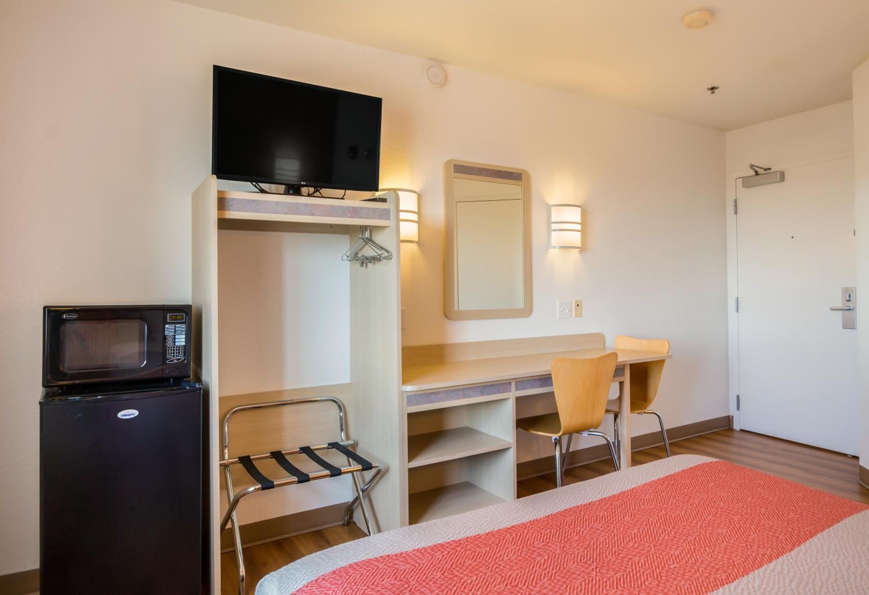 Een hotelkamer met een bed, een bureau, een stoel, een televisie, een magnetron en een spiegel.