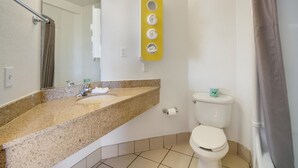Un baño con lavamanos de encimera de granito, inodoro y cortina de ducha.