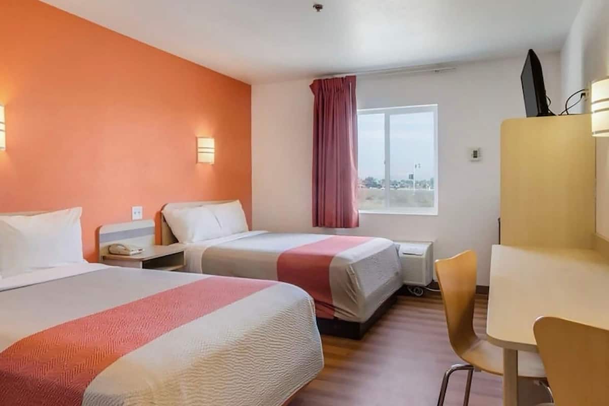 A hotel room with two beds, a desk, a chair, a window with curtains, and a city view.