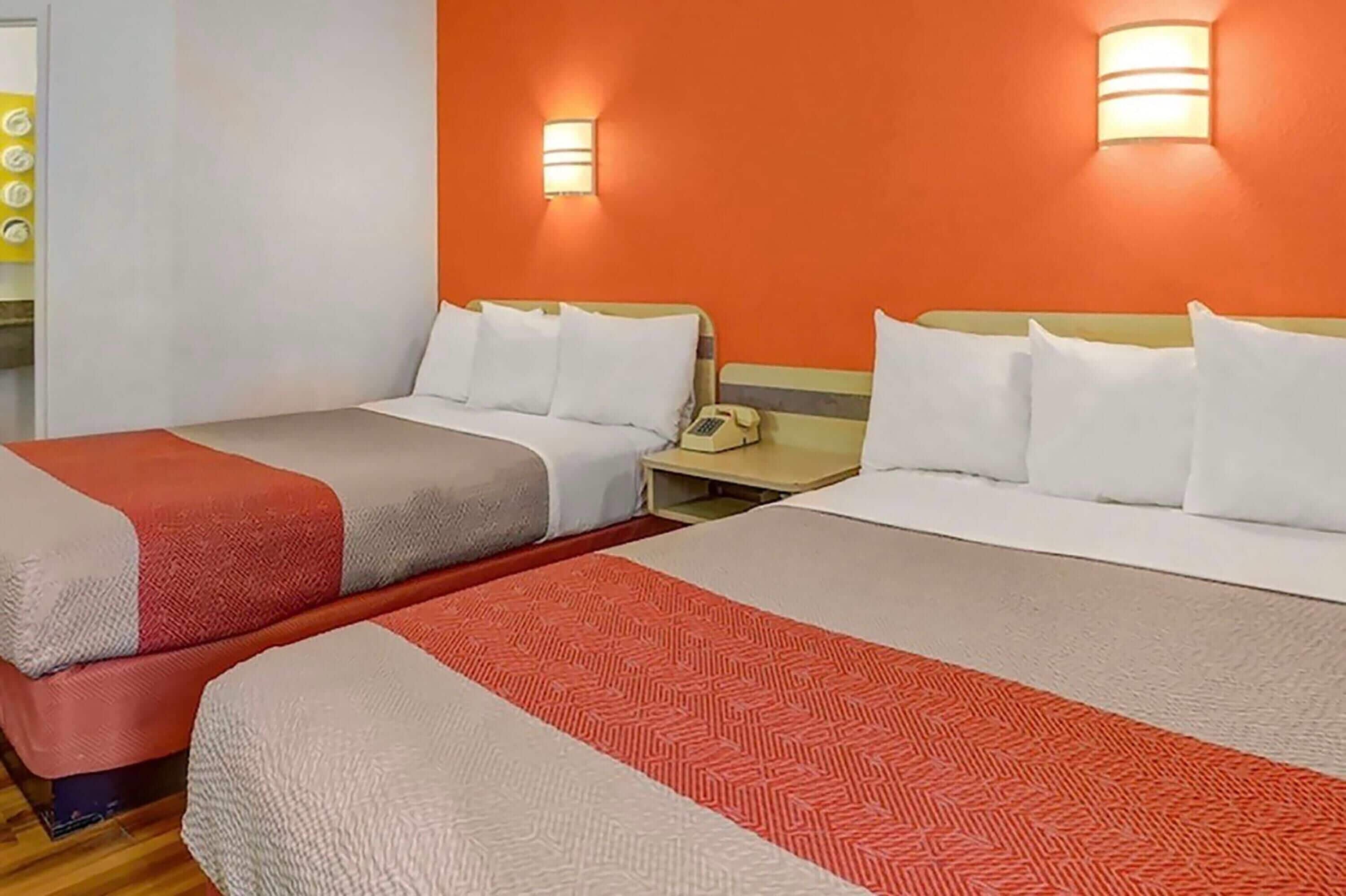 Dos camas con ropa de cama blanca y roja, un teléfono en la mesita de noche y luces fijadas a la pared.