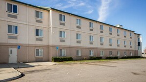 Un hotel de varios pisos con fachada plana, múltiples ventanas y un estacionamiento al frente.