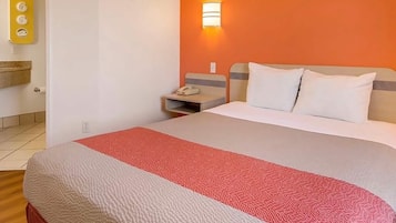Habitación de hotel con cama, mesita de noche, lámpara fijada a la pared y baño con toallero.