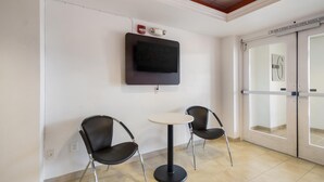 Un área de espera con dos sillas negras, una mesita redonda, un televisor de pantalla plana montado en la pared y un letrero de salida.